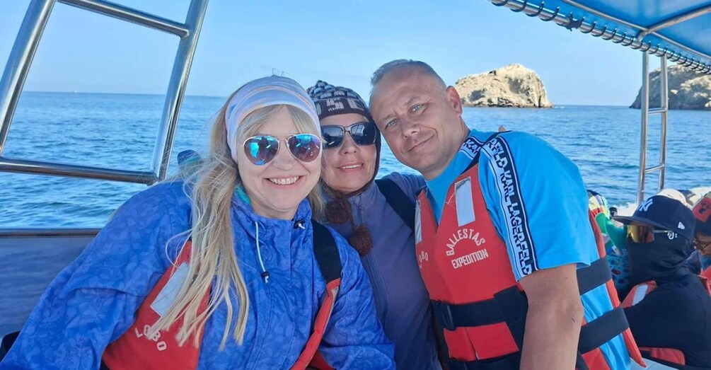 Tres personas en un bote, usando chalecos salvavidas con la inscripción 'Ballestas Expedition'. 3