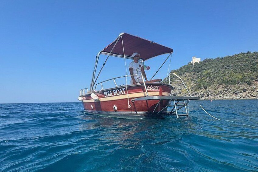 A boat named 'BOIA BOAT' anchored in the water with a clear sky and a rocky hill in the background. 4