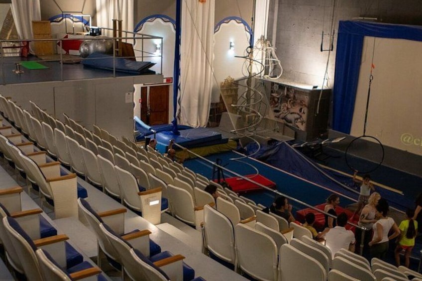 An indoor gymnasium with a gymnastics apparatus, a trampoline, and a seated audience. 4