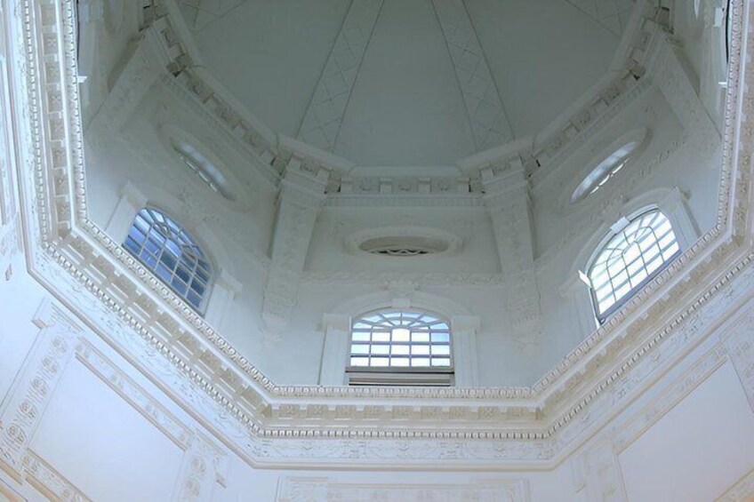 An ornate interior with a domed ceiling, decorative moldings, and arched windows. 3