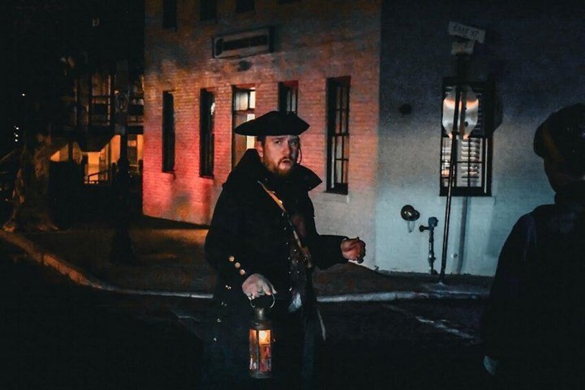 A person in a dark coat holding a lantern on a dimly lit street at night. 2