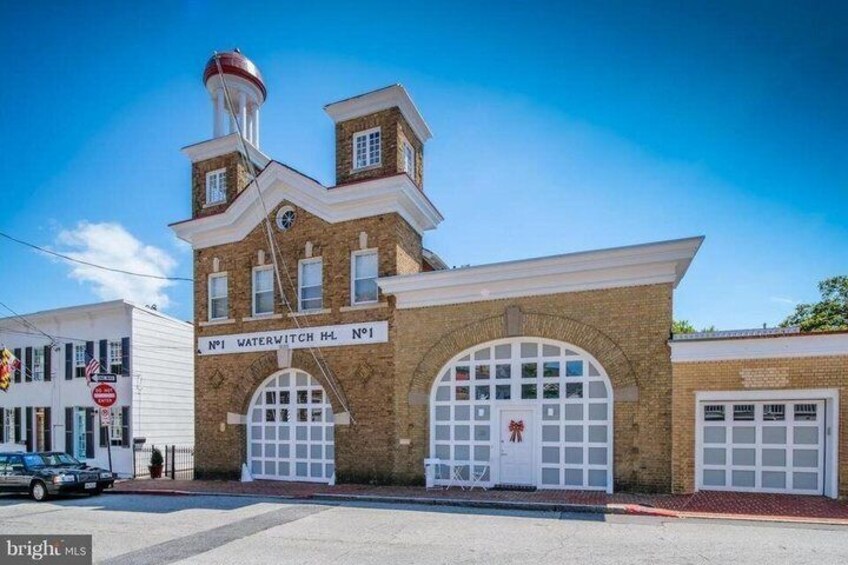 A historic fire station with two large arched garage doors, a red water tower, and a clock on the tower. 2