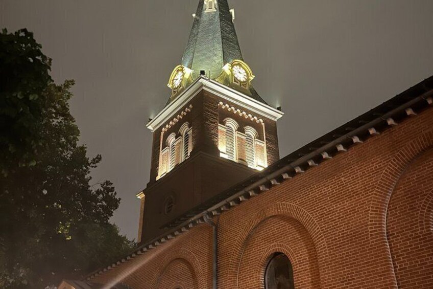 A brick building with a clock tower, arched windows, and a pointed roof. 5