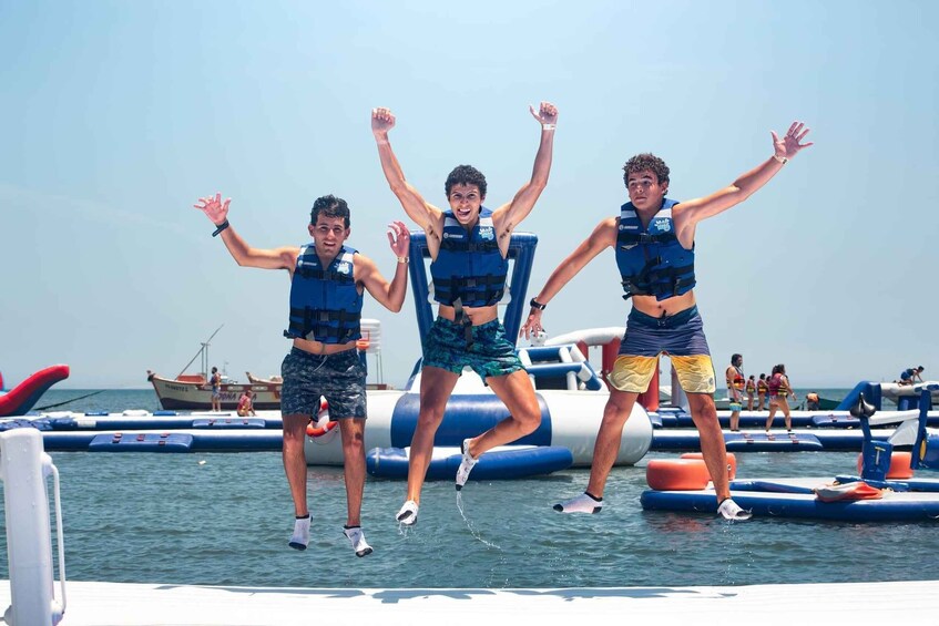 Three people jumping off a dock into the water, wearing life jackets. 1