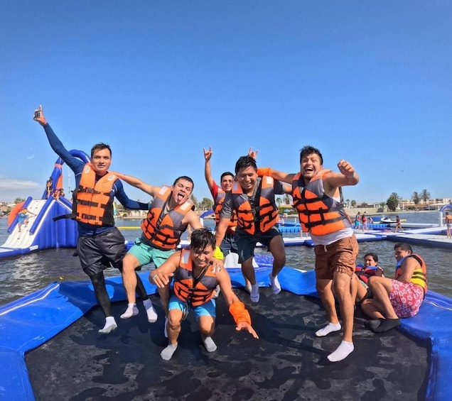 People on a watercraft wearing life jackets, with inflatable slides and a clear sky in the background. 2