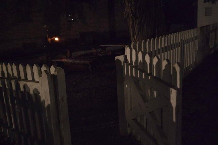 A gated area at night with a white picket fence and a dimly lit street. 2