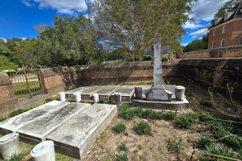 A cemetery with headstones and a prominent cross, surrounded by a brick wall and greenery. 3