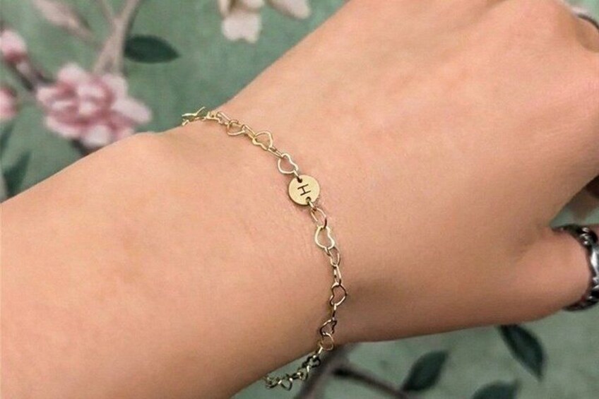 A person's arm wearing a gold bracelet with a heart-shaped pendant. 4