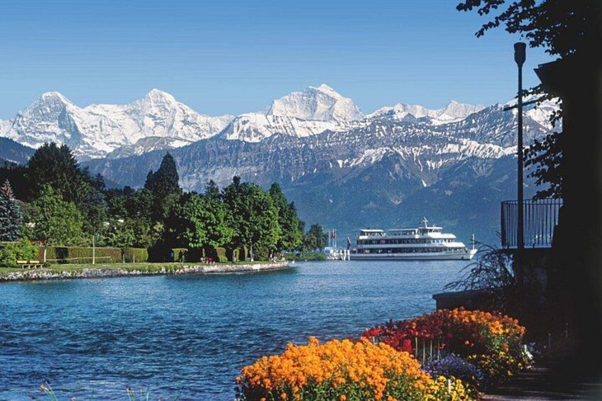 A lake with a boat, mountains in the background, and colorful flowers in the foreground. 1