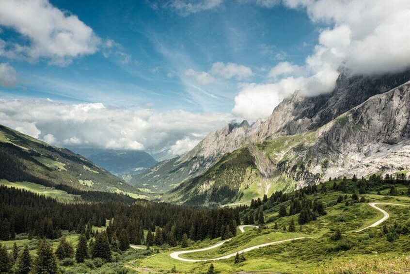 A mountainous landscape with a winding road, dense forests, and a valley. 4