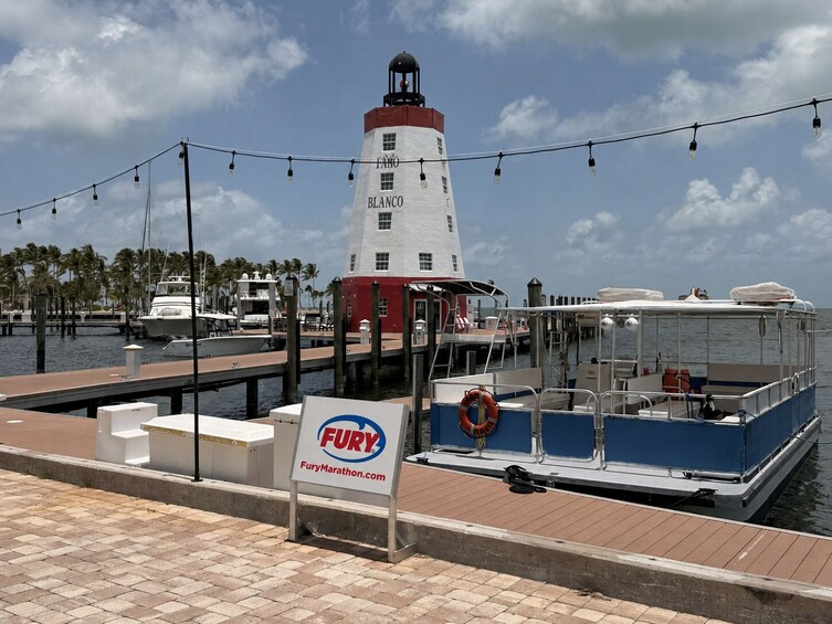 Ein Yachthafen mit einem weißen und roten Leuchtturm namens 'Blanco', einem blauen Boot, das an der Pier festgemacht ist, und einem Schild für 'FuryMarathon.com'. 3