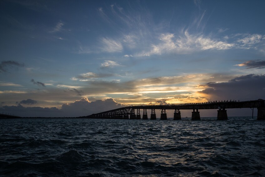 Eine Brücke über Wasser, im Hintergrund ein Sonnenuntergang. 1
