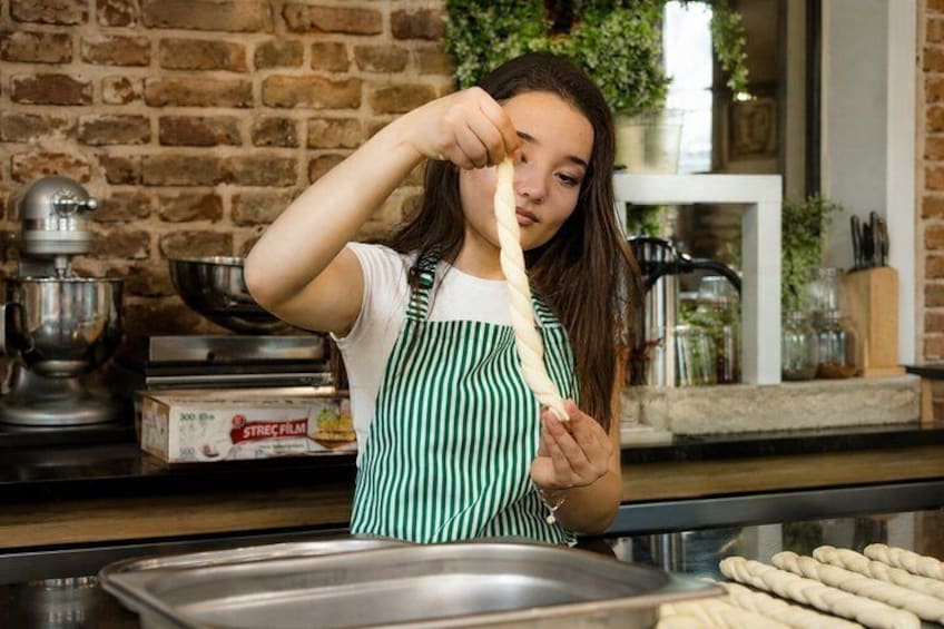 Una persona en una cocina, con un delantal verde, sosteniendo un palo de masa. 2