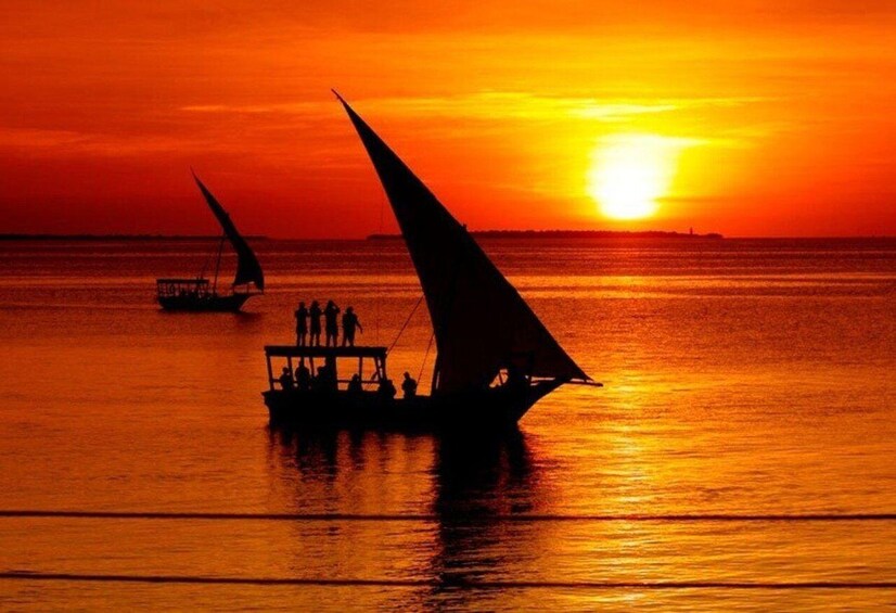 A sunset over a calm sea with two sailboats, one with a larger sail and a smaller one with people on it. 2