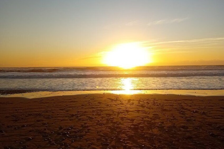 A beach at sunset with the sun low on the horizon, reflecting on the water. 1