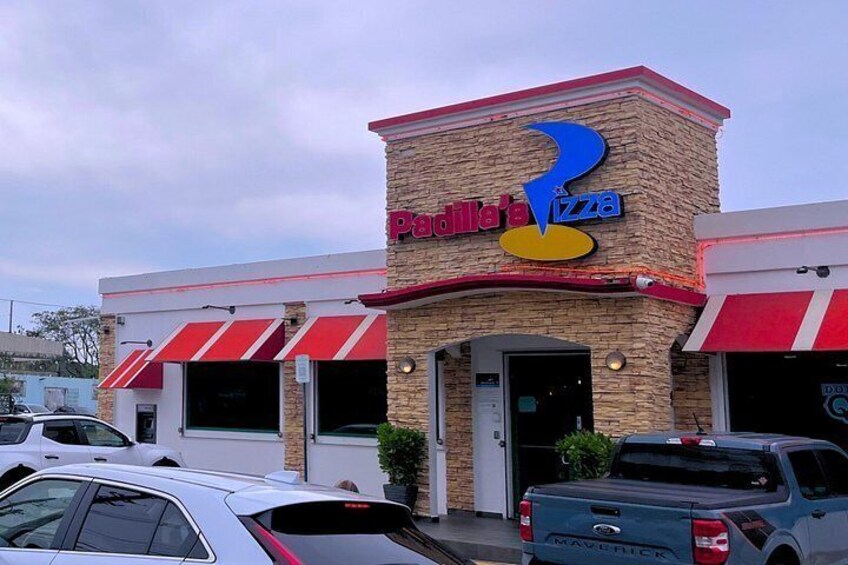 A pizza restaurant with a red and white awning, a brick facade, and a parked truck in front. 3