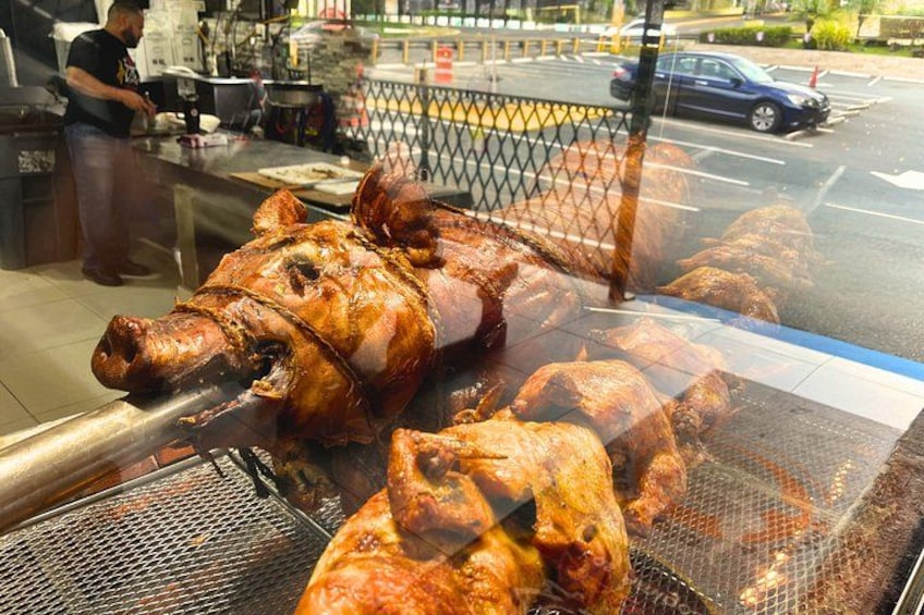 A large roasted pig on a spit, with a metal grill and a fence in the background. 3