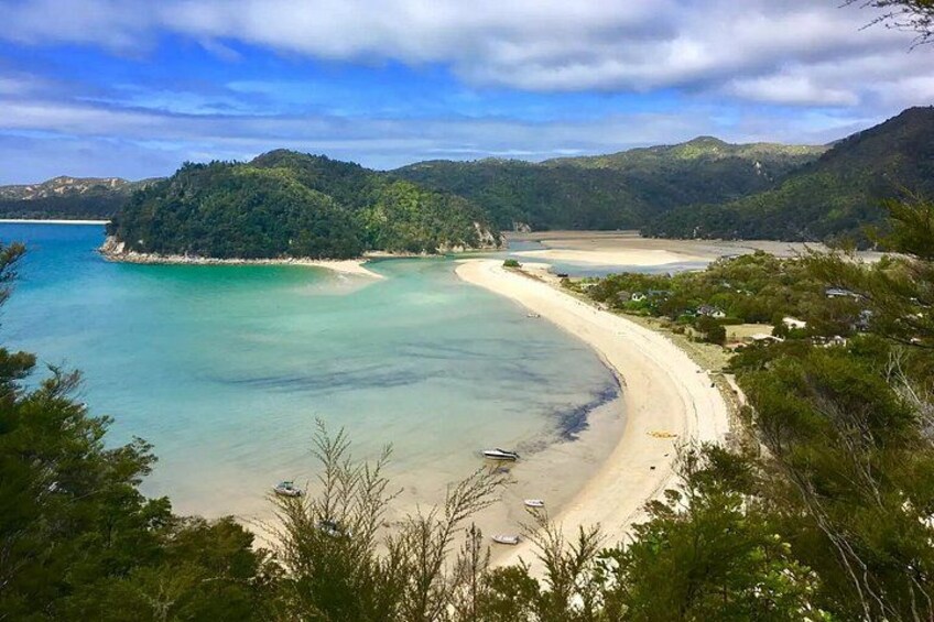 A coastal landscape with a sandy beach, clear turquoise waters, and a forested island. 2