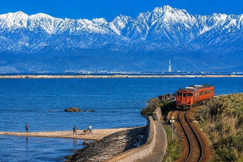 A train on tracks near a body of water with mountains in the background. 1