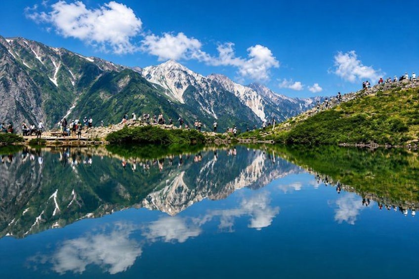 A mountain lake with reflections, a clear sky, and a group of people on a grassy hill. 3