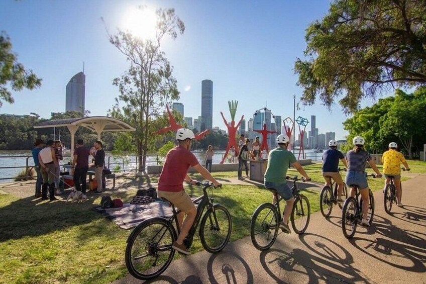 Personas pedaleando por un sendero, un área de picnic y un horizonte urbano al fondo. 3