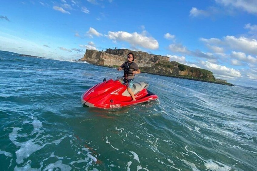 A person on a red jet ski in the ocean with a rocky coastline in the background. 4