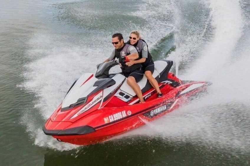 Two people on a red Yamaha jet ski moving through water. 1