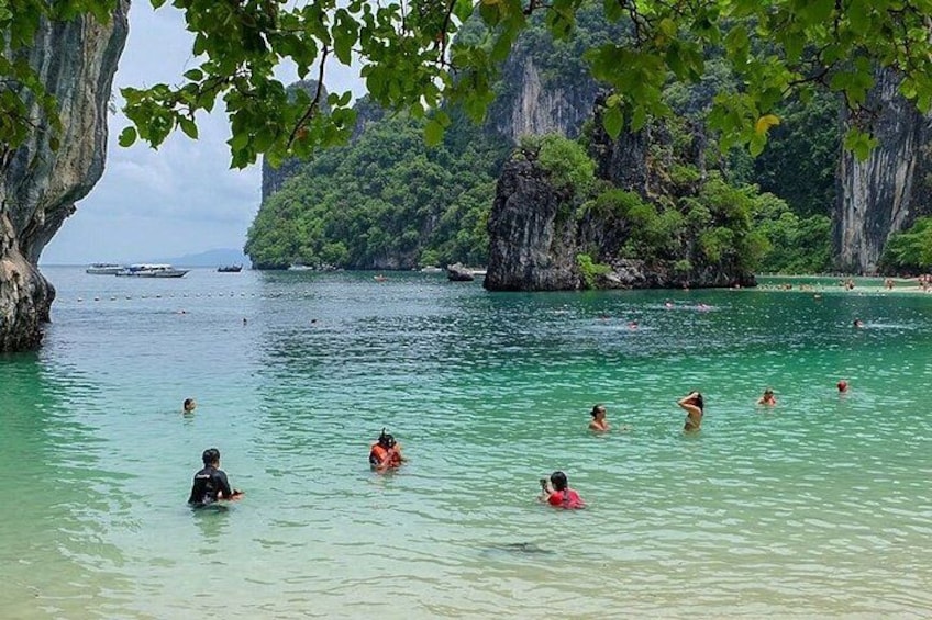 A tropical beach with clear turquoise water, people swimming, and rocky cliffs in the background. 4