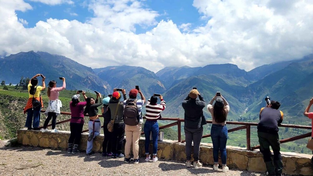 Un grupo de personas tomando fotos en un mirador con montañas al fondo. 2