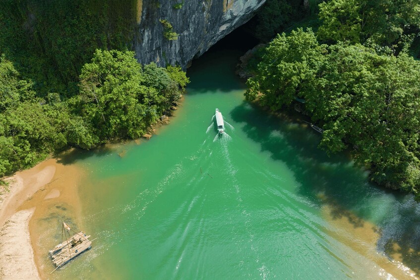 A river with a boat creating ripples, surrounded by dense green foliage and a rocky cliff. 1
