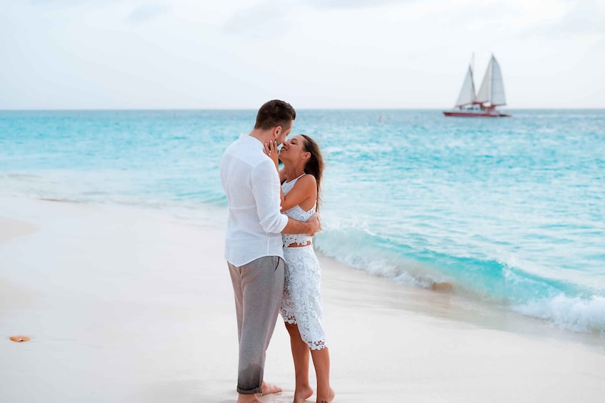A couple embracing on a beach with a sailboat in the background. 1
