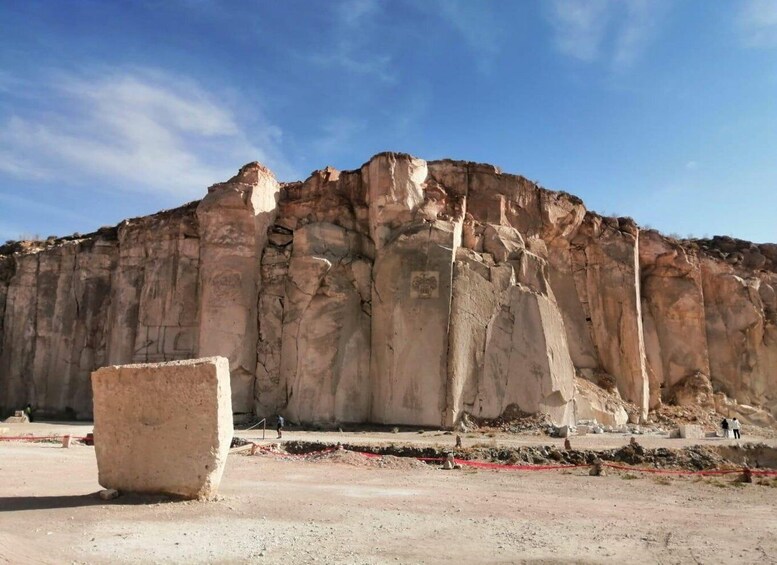 Una gran formación rocosa con cima plana y laderas escarpadas, un enorme bloque de piedra en primer plano y un cielo azul despejado. 1