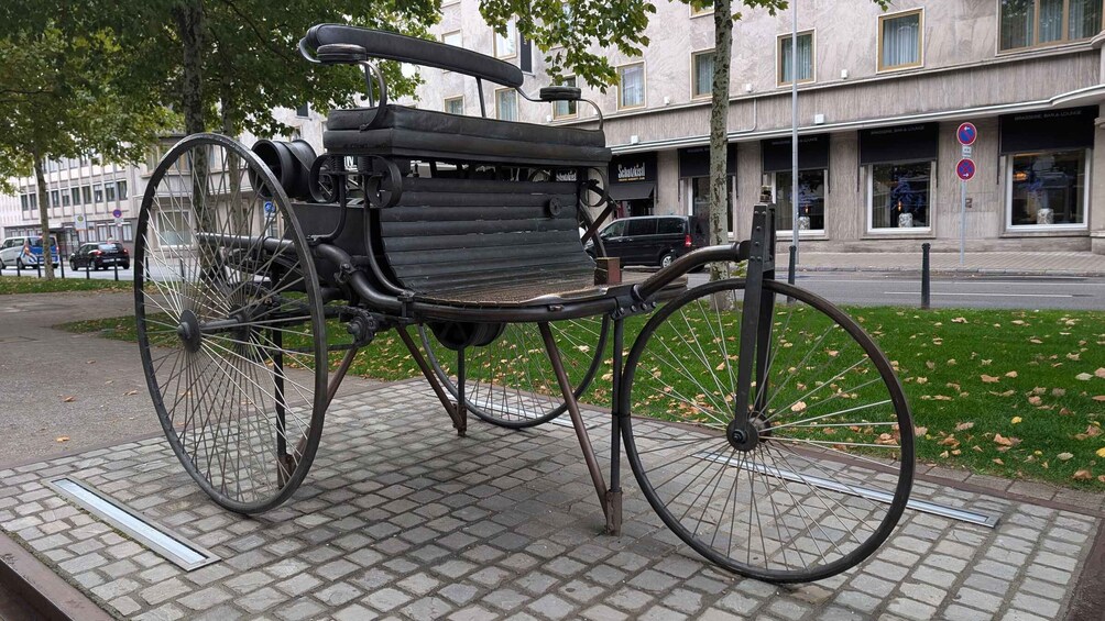 A stationary bicycle with a bench seat, parked on a paved area with a building in the background. 3