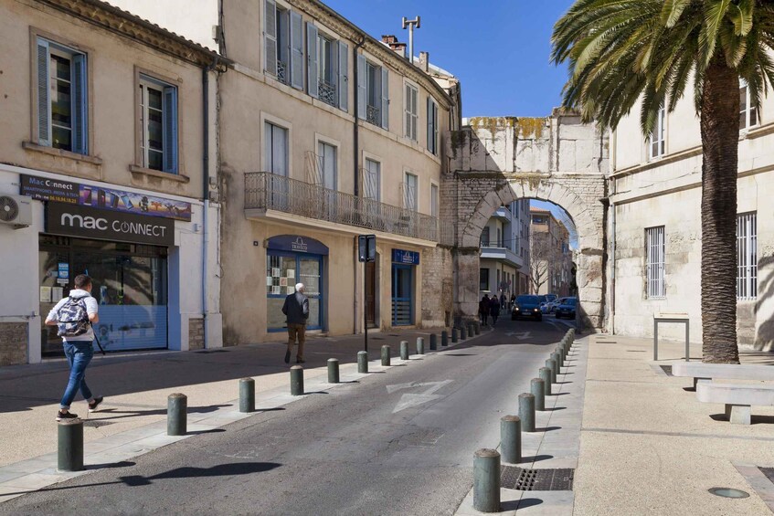 A street with buildings, bollards, and pedestrians. 1