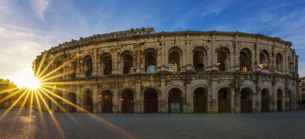 An ancient amphitheater with multiple arches and columns, under a clear sky with the sun setting or rising. 5