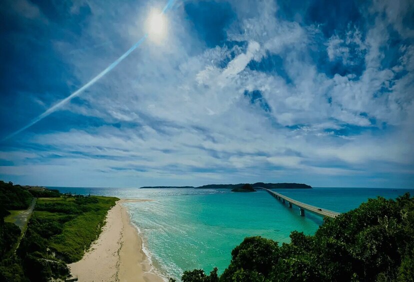 A beach with a bridge over turquoise water, a clear sky, and distant land. 3