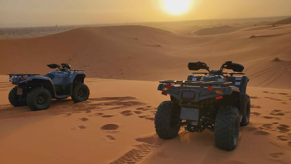 Two off-road vehicles in a desert landscape with sand dunes and a setting sun. 3