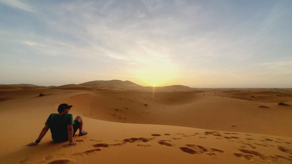 A person sitting on a sand dune with footprints leading to the horizon. 5
