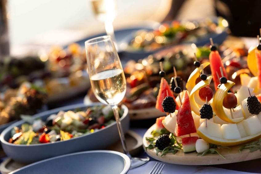 A table with various dishes, including a salad, fruit skewers, and a glass of white wine. 5