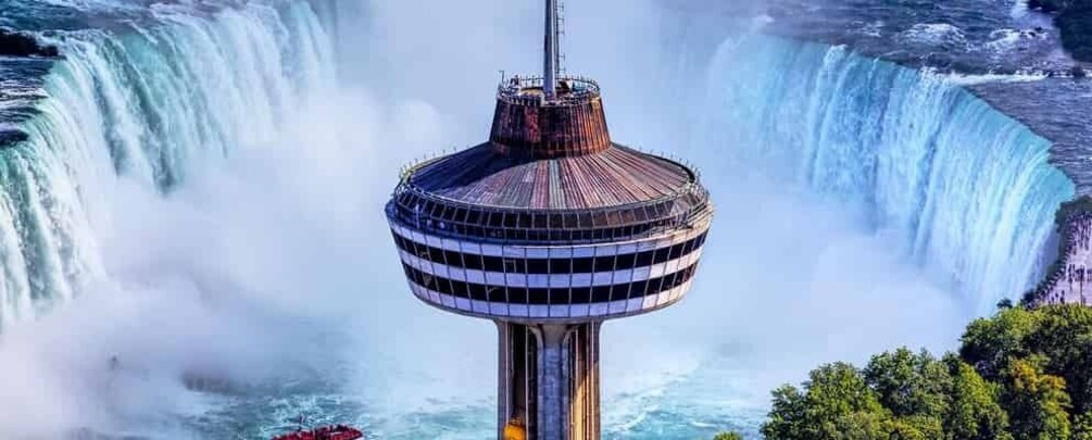A tower with a circular observation deck, a waterfall in the background, and a forested area at the base. 1