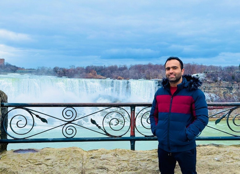 A person standing in front of a waterfall with a metal railing. 5