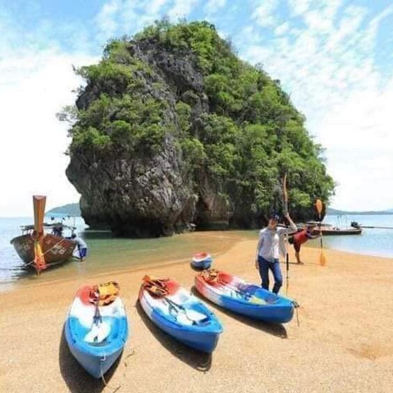 A beach with kayaks, a large rock formation, and a person paddling. 4