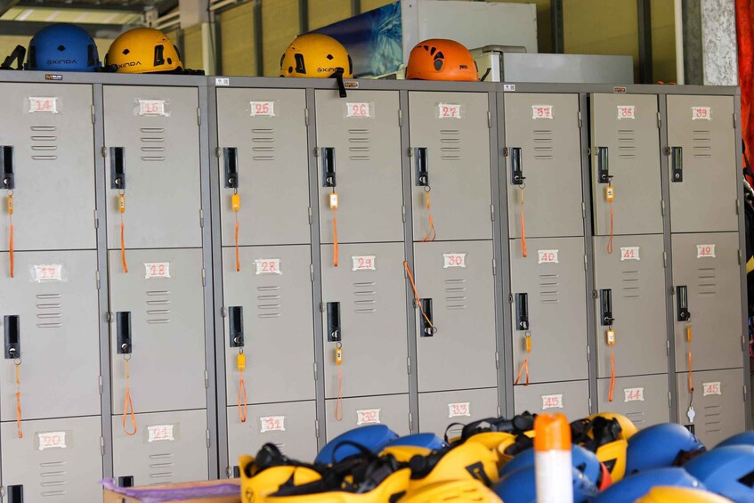 A row of lockers with numbered tags, some helmets on top, and a pile of helmets in the foreground. 5
