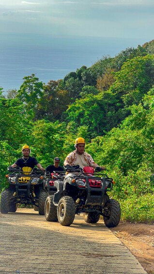 Three people riding quad bikes on a dirt road surrounded by lush greenery. 4