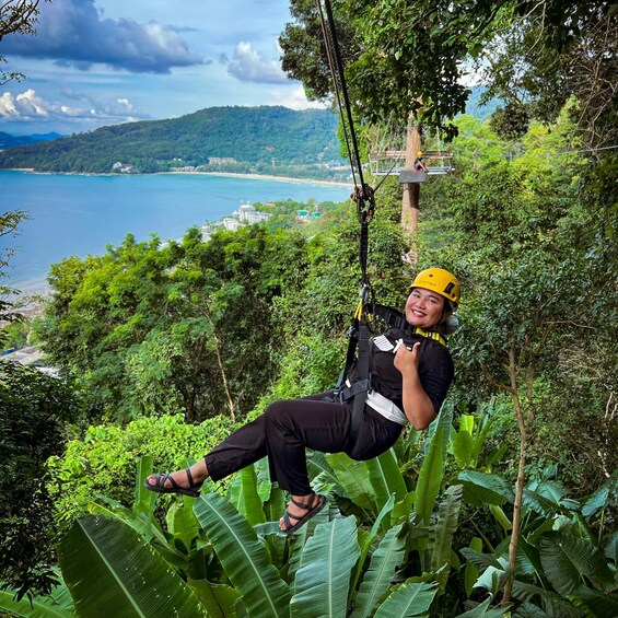 A person zip-lining over a lush green landscape with a view of the sea and mountains in the background. 1