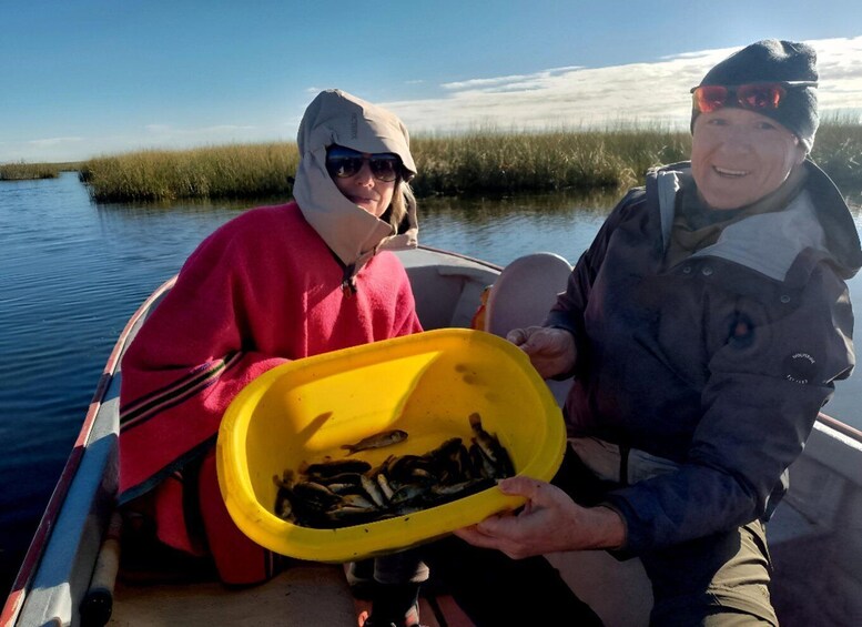Dos personas en un bote sosteniendo un recipiente amarillo con pescado. 1