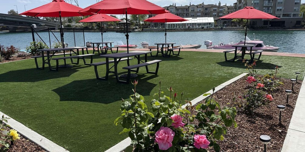 A waterfront patio with red umbrellas, picnic tables, and boats. 2