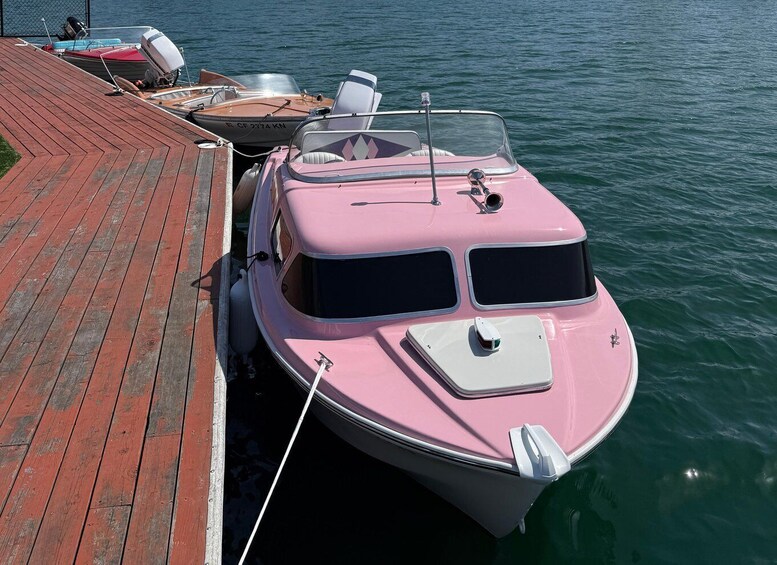 A pink boat docked at a wooden pier with calm water. 5