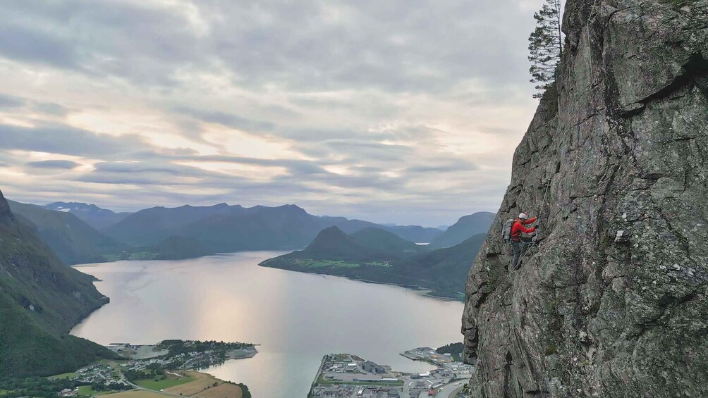 A climber on a steep cliff with a view of a lake and mountains in the background. 1