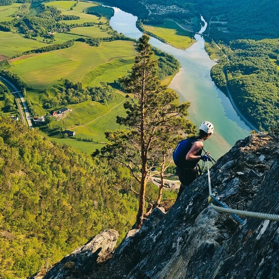A person rappelling down a cliff with a river and fields in the background. 3